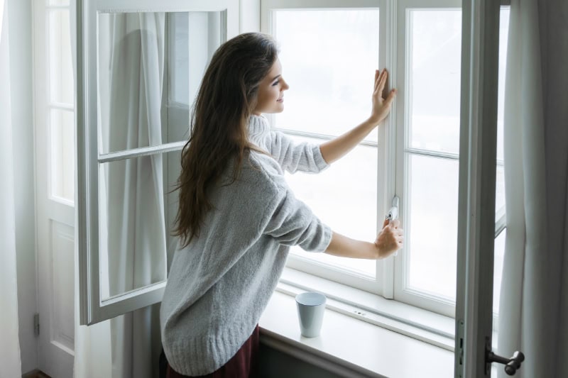 Woman in warm woolen pullover opening window of her Lock Haven, PA, home.