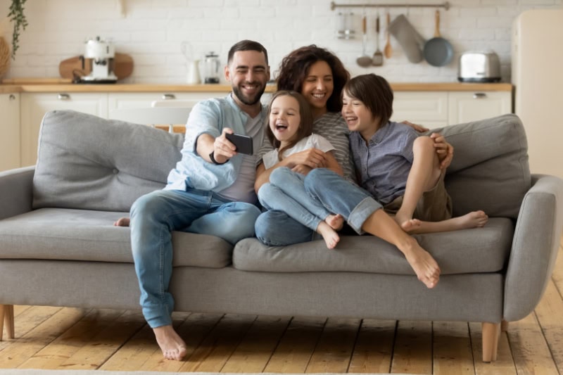 What Are Signs I Need a New Furnace? Family of four laughing and playing on their couch, posing for a photo.