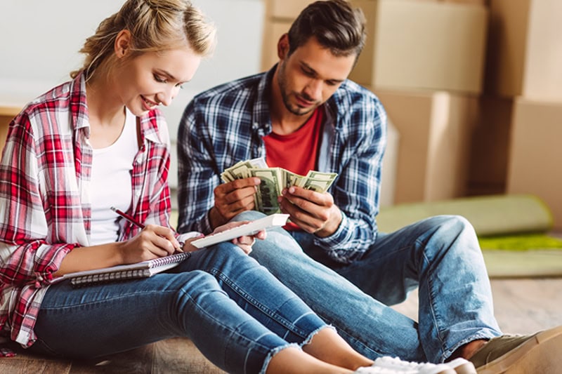 2025 Is Your Last Chance to Claim Federal HVAC Tax Credits. Young couple counting money while sitting on floor in new apartment.