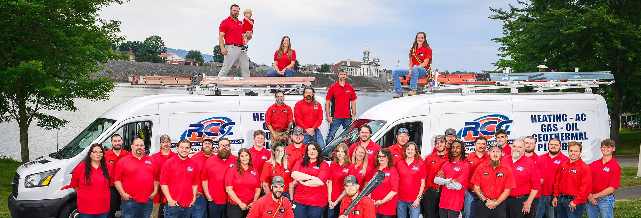 RCC Mechanical team in front of two HVAC and plumbing service vehicles. Some employees standing or sitting on top of service vehicles.