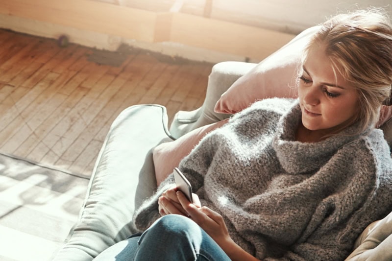 Shot of a young woman relaxing on the sofa at home and using a mobile phone.